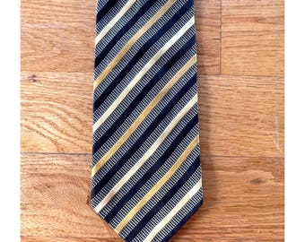 Puede incluir: Una corbata con un patrón repetitivo de rayas diagonales en negro, dorado y blanco. Las secciones negras tienen una textura de cuadrícula fina con pequeños puntos blancos, mientras que las rayas doradas y blancas son lisas.