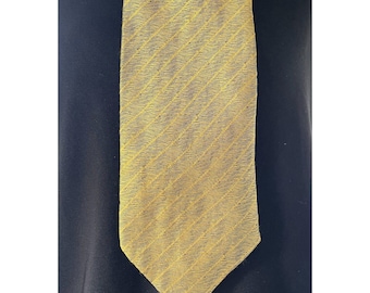 Puede incluir: Una corbata dorada con un patrón sutil de finas rayas diagonales en toda la superficie. La corbata tiene un extremo puntiagudo y una apariencia texturizada, presentada sobre un fondo negro sólido para resaltar el color metálico.