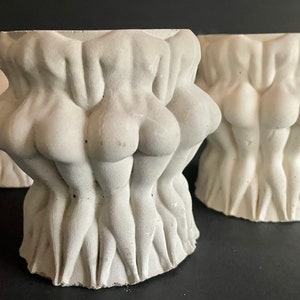 May include: Three white ceramic planters shaped like a group of figures standing together. The planters are made of a rough, textured material and have a slightly distressed look.