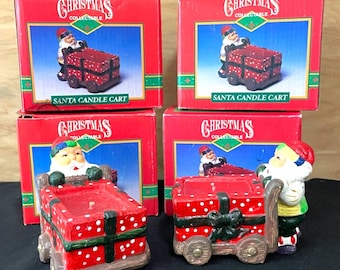 Puede incluir: Dos figuras de carrito de vela de Santa Christmas Collectable con sus cajas rojas. Cada figura muestra a un Santa Claus empujando un regalo rojo con puntos blancos sobre ruedas, que funciona como un portavelas.