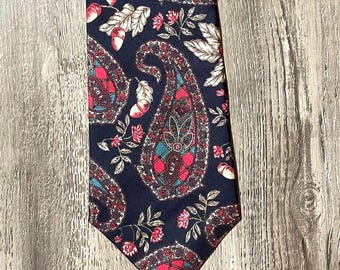 Puede incluir: Una corbata con fondo azul marino oscuro y un patrón repetitivo de grandes formas de cachemira en tonos rojo, verde azulado y blanco. El diseño está intercalado con pequeñas ilustraciones de bellotas y hojas de roble en tonos crema y rojo.