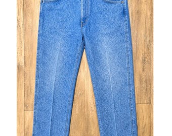 Puede incluir: Un par de vaqueros de mezclilla azul claro con lavado ácido, diseño clásico de cinco bolsillos, cierre de botones y trabillas para cinturón. El pantalón tiene un corte recto con costuras verticales visibles en cada pierna.