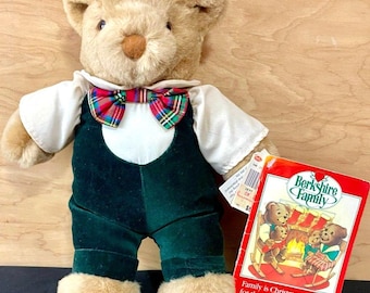 Puede incluir: Un oso de peluche color canela con camisa blanca, peto de terciopelo verde oscuro y pajarita de cuadros rojos, verdes y azules. Una etiqueta rectangular adjunta muestra el texto Berkshire Family y una ilustración de osos.