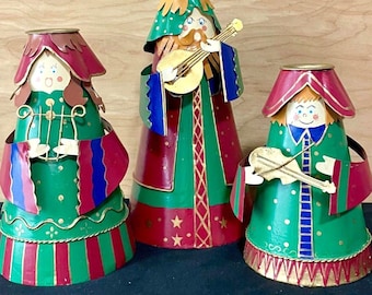 Puede incluir: Tres figuras de metal en forma de cono que representan músicos con túnicas verdes, rojas y azules. La figura de la izquierda sostiene una lira, la del centro toca un laúd y la de la derecha sostiene un violín. Cada figura tiene un rostro pintado.
