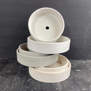May include: A stack of four white and gray ceramic planters of varying sizes. The planters are stacked in a pyramid shape, with the largest planter at the bottom and the smallest planter at the top.