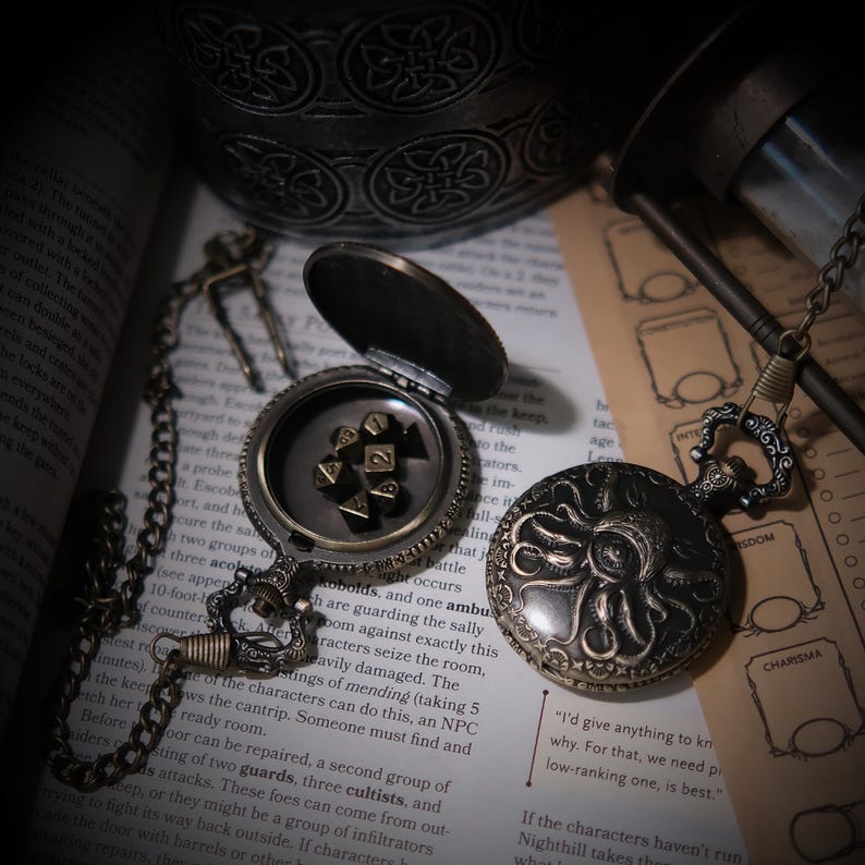 K&ouml;nnte beinhalten: Zwei Taschenuhren aus Bronze im antiken Stil mit komplizierten Krakenmotiven auf den Deckeln. Eine Uhr ist ge&ouml;ffnet und zeigt ein Set kleiner metallischer polyedrischer W&uuml;rfel im Inneren. Beide Uhren haben verzierte Metallketten.