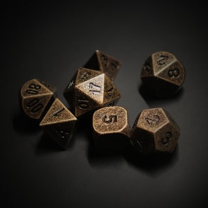 May include: A set of seven antique bronze-colored polyhedral dice, including a D4, D6, D8, D10, D12, D20, and a percentile die. The dice are arranged on a dark surface, with numbers clearly visible.