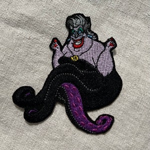May include: Embroidered patch featuring a cartoon depiction of Ursula, the sea witch. The patch showcases Ursula's purple skin, black tentacles, and a sinister grin. The design includes details like her gray hair, red nails, and a golden shell necklace.