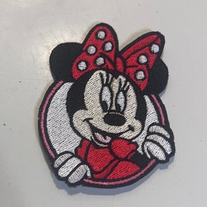 May include: A red and white embroidered patch featuring a cartoon image of Minnie Mouse with a red bow and white polka dots.