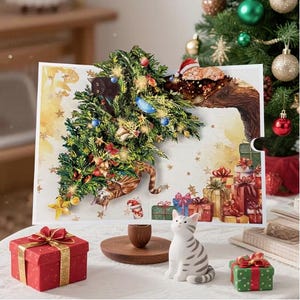 May include: A Christmas pop-up card with a decorated tree and cats, alongside wrapped gifts. A ceramic cat figurine and presents are on the table. The card has a festive design with gold detailing, creating a whimsical scene.
