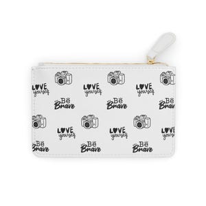 May include: White zippered pouch featuring a repeating pattern of black cameras, hearts, and the phrases "Love Yourself" and "Be Brave." It has a gold zip and a white pull tab.