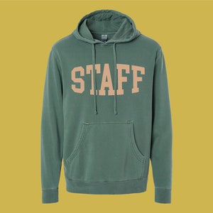 Puede incluir: Una sudadera con capucha verde con la palabra "STAFF" impresa en color melocotón en la parte delantera.