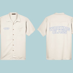 Op de afbeelding: Een wit, kort mouwig overhemd met knopen en een zakje aan de linkerkant. Op de achterkant staat in blauw "WORKING CLASS" gedrukt.