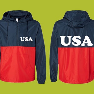 May include: A navy blue and red anorak jacket with a hood and a front pocket. The word "USA" is printed in white on the front and back of the jacket. The jacket is made of a lightweight material.