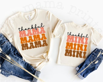 Può includere: Due magliette beige con un design di font retrò. La maglietta più grande dice "thankful mama" in testo sovrapposto. La maglietta più piccola dice "thankful mini" in testo sovrapposto.