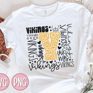 May include: White t-shirt with a black and yellow design featuring the word "Vikings" repeated in different styles and sizes. The design includes a large yellow "V" with a leopard print pattern.