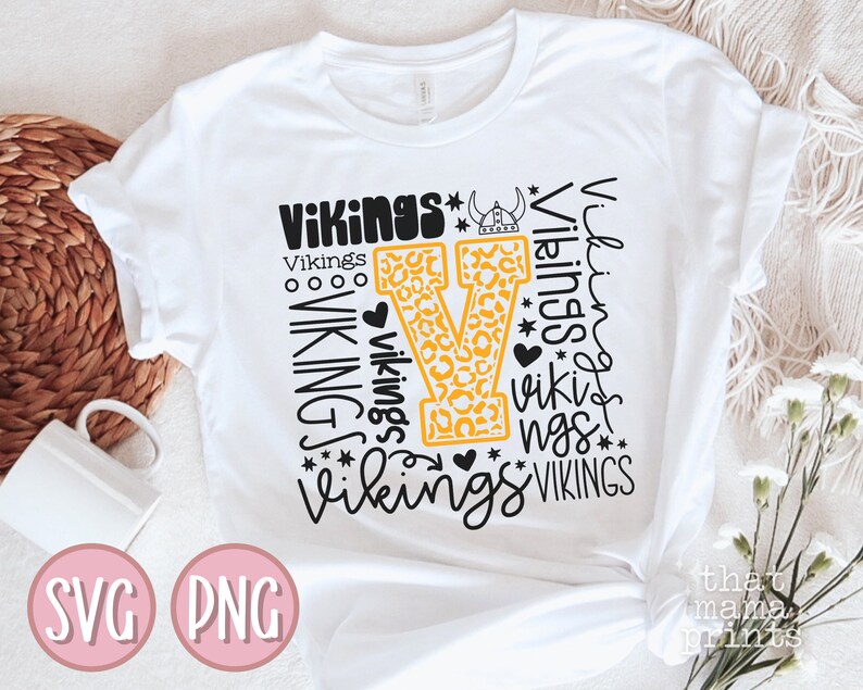 May include: White t-shirt with a black and yellow design featuring the word "Vikings" repeated in different styles and sizes. The design includes a large yellow "V" with a leopard print pattern.