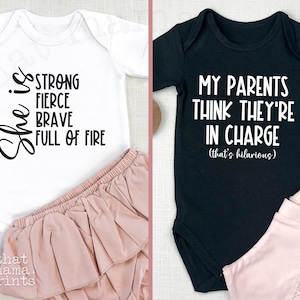 May include: Two baby onesies, one white with black text that reads "She is strong fierce brave full of fire" and one black with white text that reads "My parents think they're in charge (that's hilarious)"