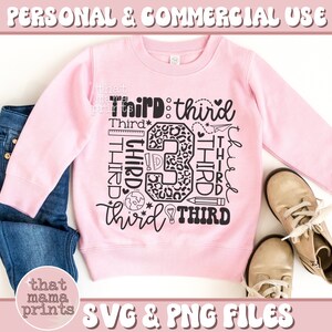 May include: Pink sweatshirt with a black graphic design that says "Third" multiple times in different fonts and styles. The graphic also includes a number 3 with a leopard print pattern and school supplies like a pencil, ruler, and lightbulb.