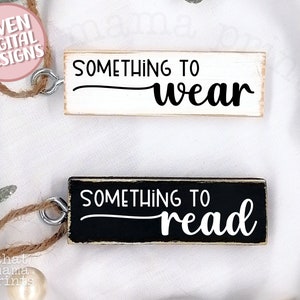 May include: Two wooden signs with black text. The top sign is white with the text "Something to wear". The bottom sign is black with the text "Something to read".