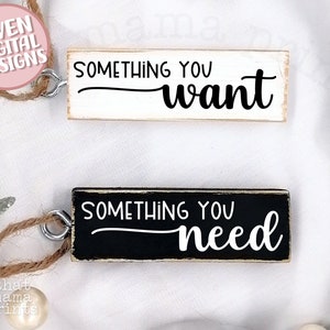 May include: Two wooden signs with black and white text. The top sign is white with black text that reads "Something you want". The bottom sign is black with white text that reads "Something you need".