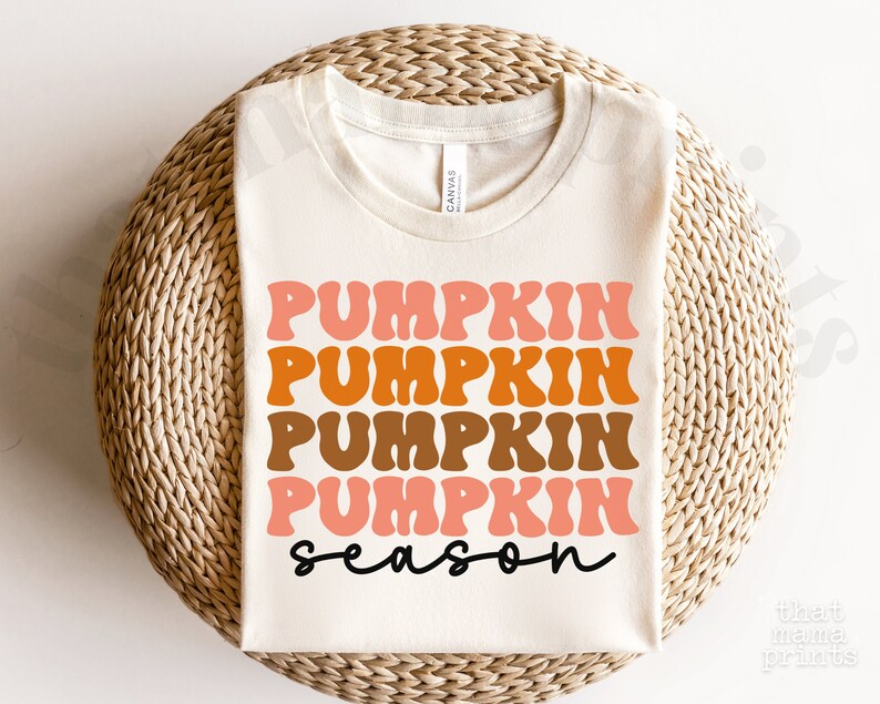 May include: A white t-shirt with the text "Pumpkin season" in a retro font. The text is in shades of orange, brown, and pink.