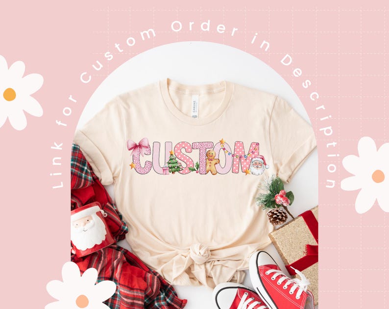 May include: A beige t-shirt with a pink and white "CUSTOM" design featuring Christmas-themed elements like a gingerbread man, a Christmas tree, and a Santa Claus. The design is surrounded by pink polka dots and a pink bow.