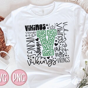 May include: White t-shirt with a green and black design featuring the word "Vikings" repeated in different styles and sizes. The design includes a large green "V" with a leopard print pattern.