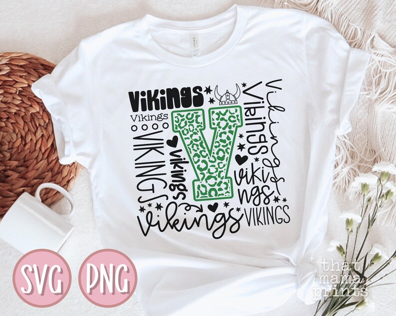 May include: White t-shirt with a green and black design featuring the word "Vikings" repeated in different styles and sizes. The design includes a large green "V" with a leopard print pattern.
