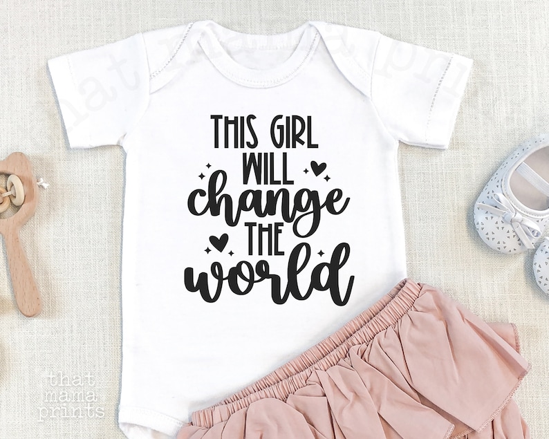 May include: White baby onesie with black text that reads "This girl will change the world".
