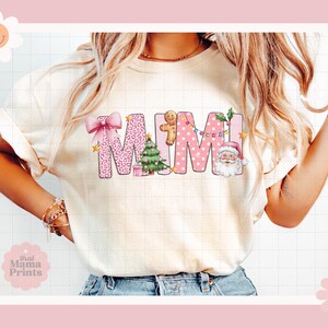 May include: A white t-shirt with a pink and white "MIMI" design featuring a gingerbread man, a Christmas tree, and a Santa Claus. The design has a pink polka dot pattern and a leopard print.