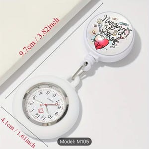 Könnte beinhalten: Weißer einziehbarer Ausweishalter mit einer weißen analogen Uhr und einem farbenfrohen Design, auf dem "Nursing is a work of heart" steht. Der Ausweishalter hat einen Durchmesser von 9,7 cm und die Uhr einen Durchmesser von 4,1 cm. Modell: M105