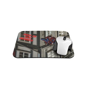May include: A mouse pad featuring a Spiderman graphic with the text "Soar to New Heights" in red. The background is a photo of a building with windows.
