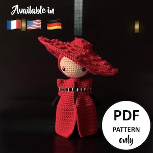 Peut inclure: Une poupée rouge au crochet faite à la main, portant un chapeau et un manteau assortis. La poupée a un visage beige et des yeux noirs. L'image comprend le texte "Available in" avec les drapeaux français, américain et allemand, et un cercle blanc avec "PDF PATTERN only".