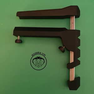 May include: Black plastic VR headset stand with two adjustable arms and a silver metal rod. The stand has a logo that says "KOBRA VR" with a snake design.