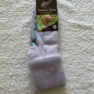 May include: A pair of lavender fuzzy socks with a blue non-slip tread. The socks have a tag that reads "Comfort Socks Made in New Zealand Since 1980 One Size Non Slip Tread".