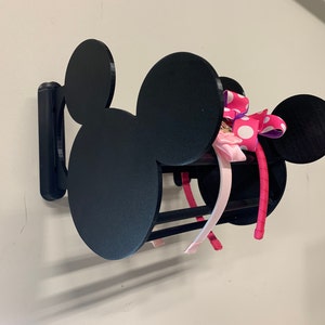 May include: Black Mickey Mouse-shaped wall-mounted headband holder with pink and white polka dot headbands and a pink bow.