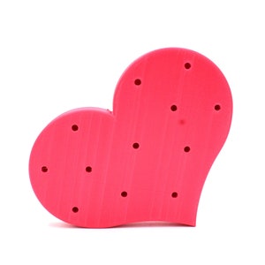 May include: A bright pink heart-shaped cake stand with multiple holes for inserting cake pops or other treats.
