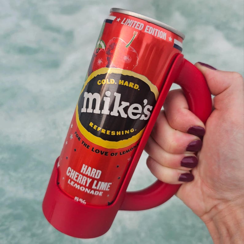 May include: A red can of Mike's Hard Cherry Lime Lemonade in a red handle holder. The can has the text "LIMITED EDITION", "COLD. HARD.", "mike's", "REFRESHING.", and "HARD CHERRY LIME LEMONADE". The drink is 5% alcohol.