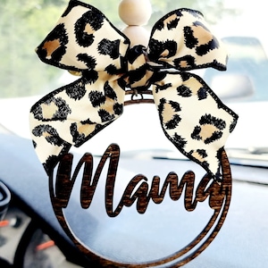 May include: A wooden car charm with the word "Mama" in cursive script. The charm is decorated with a brown and black leopard print bow and wooden beads.