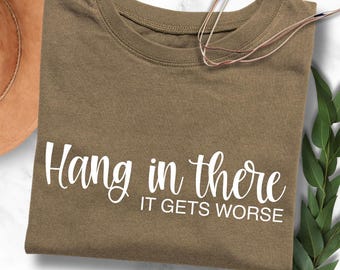 May include: A brown t-shirt with the text "Hang in there it gets worse" printed in white.