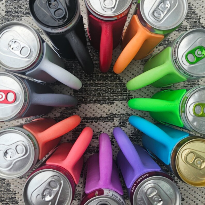 May include: An overhead shot of a circle of aluminum cans with colorful can holders attached. The holders are in various colors, including black, red, orange, green, blue, pink, and purple. The cans are silver with pull tabs.
