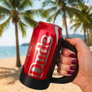 May include: A red Coca-Cola can with the word "Dude" in white script, held in a black handle. The can is on a beach with palm trees and the ocean in the background. The text "share a Coke with your" is also visible.
