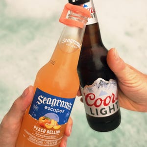 May include: Two bottles of alcoholic beverages are held up in a celebratory gesture. One is a Seagram's Escapes Peach Bellini, and the other is a Coors Light. The Seagram's bottle is orange, and the Coors Light bottle is brown.