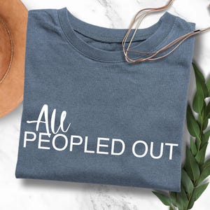 Könnte beinhalten: Ein blaues T-Shirt mit dem Text "All People Out" in weißen Buchstaben.
