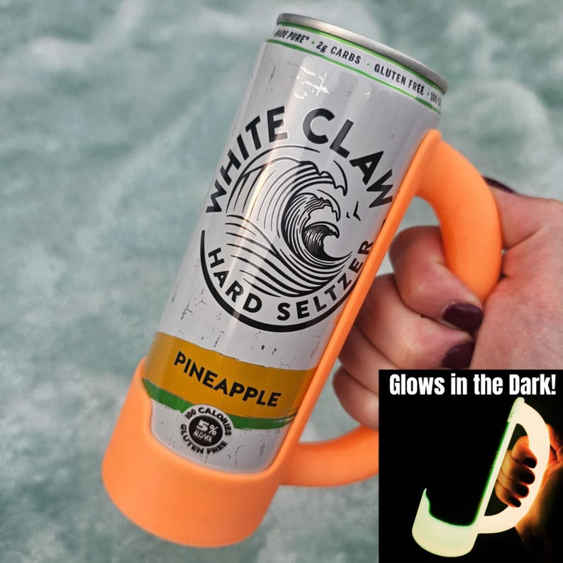 May include: A can of White Claw Hard Seltzer in a bright orange holder. The can is silver with black and white branding and a pineapple flavor label. The holder has a handle and glows in the dark.