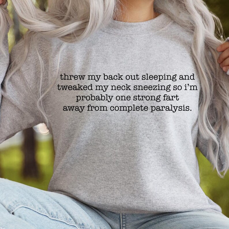 May include: Gray sweatshirt with a humorous saying: "threw my back out sleeping and tweaked my neck sneezing so i'm probably one strong fart away from complete paralysis."