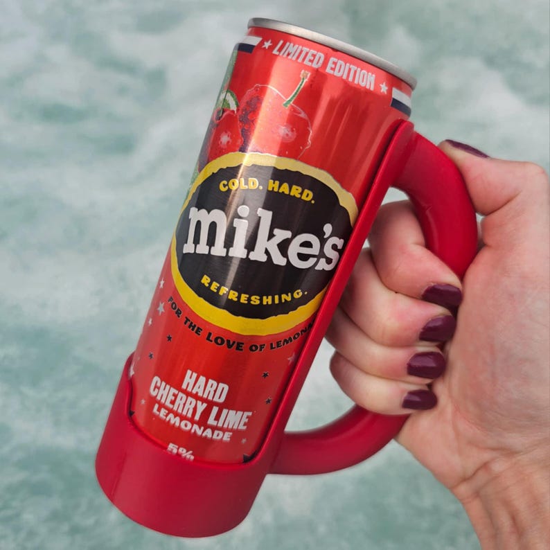 May include: A red can of Mike's Hard Cherry Lime Lemonade in a red handle. The can has the words "COLD. HARD. mike's REFRESHING" and "HARD CHERRY LIME LEMONADE" printed on it. The can is held in a red handle.