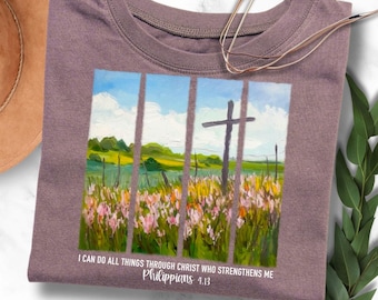 May include: A purple t-shirt featuring a painting of a field with a cross in the background. The text "I can do all things through Christ who strengthens me Philippians 4:13" is printed on the shirt.