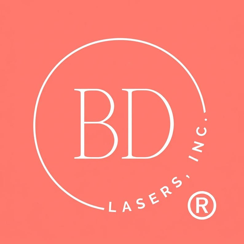 May include: A logo featuring the white capital letters "BD" inside a white circle, set against a coral background. The words "LASERS, INC." are written in white around the circle's perimeter, with a registered trademark symbol.